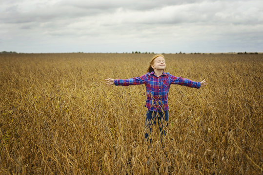 Carefree girl with arms outstretched standing amidst soybean's field against cloudy sky