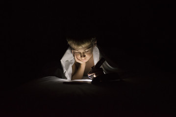 Boy reading book using flashlight in darkroom