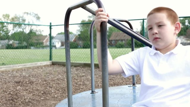 Boy spinning alone on a merry go round in playground.
