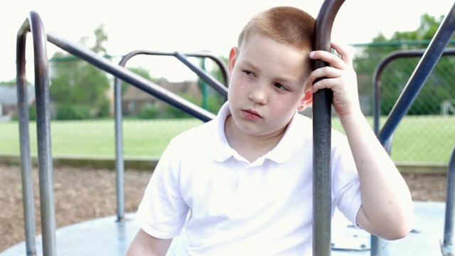 Boy leaning against bar of merry go round thinking.  He looks very sad.

