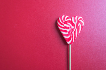 Close up and top view of red and white striped heart shaped lollipop isolated on red background, toned. Be Mine Valentine or Happy Valentine's day concept