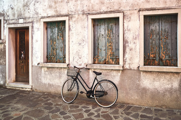 Fototapeta na wymiar Old rusty bicycle against the old wall on the street. Italy, Venice, Burano island
