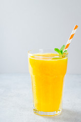 One glass of freshly pressed orange juice with a straw and mint on the background. Front view, vertical image, copy space