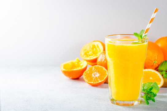 One glass of freshly pressed orange juice with a straw and oranges on the background. Front view, horizontal, copy space