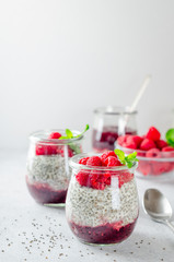 Two glass jars with chia pudding with raspberry and jam. Bowl of raspberry on the background. Vertical image, copy space, close-up, front view