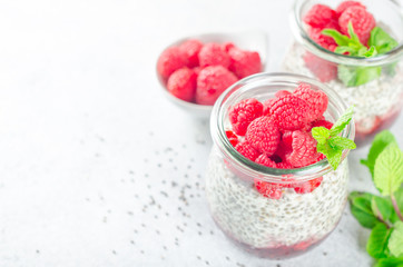 Two glass jars with chia pudding with raspberry and jam. Bowl of raspberry on the background. Horizontal image, copy space, close-up, high key
