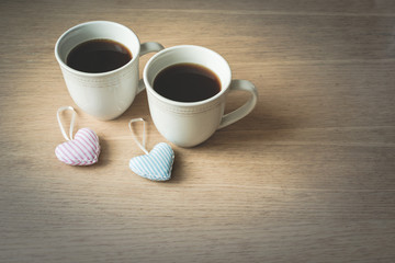 View of two white vintage coffee cups with two fabric, textile, striped pink and blue  hearts hanging from spoons on wooden background, vintage toned. Love, marriage, or Happy Valentine's Day concept