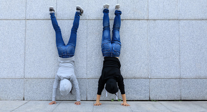 Two female hipsters doing handstand against wall in city