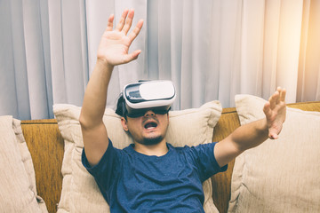 Asia man wearing and playing virtual reality enjoy in game content , sitting on brown sofa