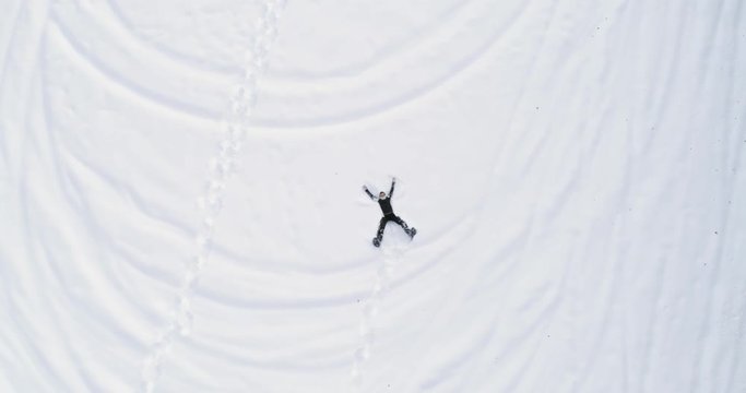 Overhead aerial top view over man lying doing snow angel with snowshoes on white covered snowy field in winter.People enjoy and have fun outdoor in nature.4k drone flight straight-down perspective