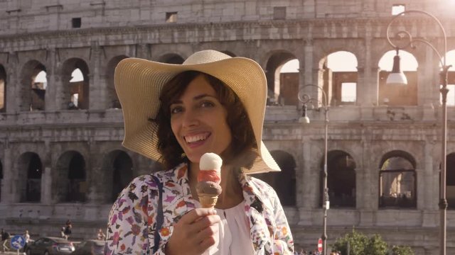 Beautiful young woman in colorful fashion dress eating ice cream in front of colosseum in Rome at sunset attractive girl with elegant straw hat