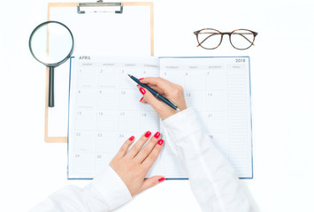 Top view office desk.  Workspace with female hands, clipboard, calendar and glasses
