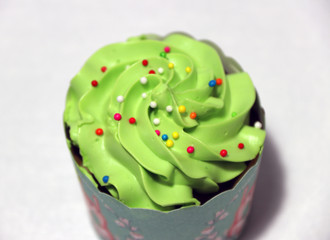 Green color of cup cake on the white background with colorful rounded sugar beads on the cream. cupcake is a small cake baked in a cup-shaped container.