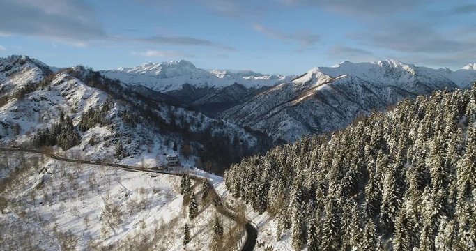 Forward aerial top view on white snow mountain pass valley in winter.Forest woods.Snowy mountains street path establisher.Sunset or sunrise sun backlit.4k drone flight straight-down establishing shot