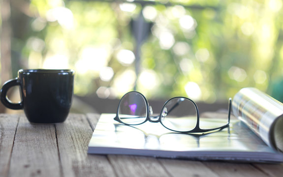 An open book, glasses and a blanket on the wooden background. orange, coffee cup, sunlight, selective focus.