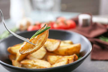 Piece of delicious baked potato with rosemary on fork, closeup