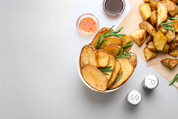 Composition with bowl of tasty rosemary potatoes on table