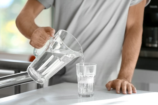 Morning of young man pouring water into glass in kitchen