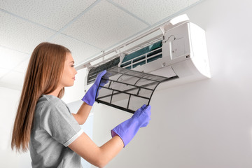 Young woman cleaning air conditioner, indoors