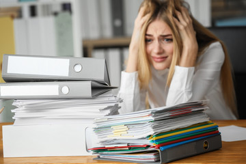 Emotional woman with stack of documents on her table in office