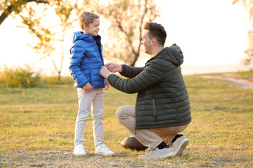 Father zipping up jacket of little son outdoors