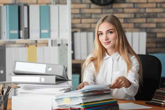 Young woman with stack of documents on her table in office