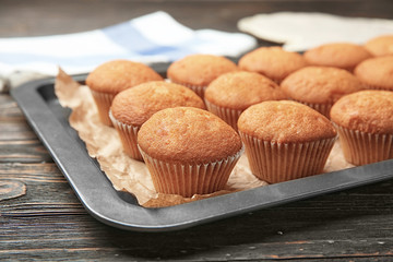 Baking sheet with delicious cupcakes on wooden table, closeup