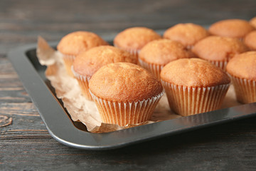 Baking sheet with delicious cupcakes on wooden table, closeup