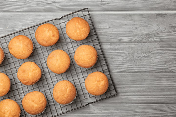 Cooling rack with delicious cupcakes on wooden background, top view