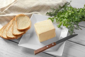 Plate with piece of fresh butter and sliced bread on table