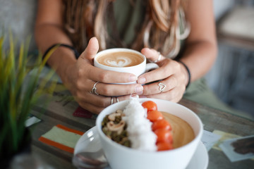 Close up female hands hold a mug of coffee. fruits and nuts bowl is in front