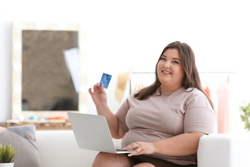 Beautiful overweight woman with laptop and credit card indoors
