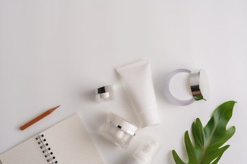 White cosmetic products and green leaves on white background. Natural beauty products for branding mock-up concept.