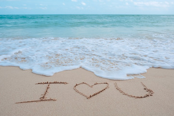 The hand writing word I love you on the beach by the sea with white waves and blue sky background