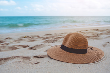 Closeup image of a sun hat or beach hat on the sand by the sea with blue sky background