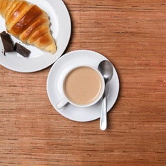 Coffee and croissant on wood background.