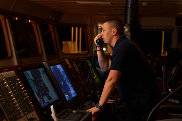 Fototapeta na wymiar Pilot / Navigator on the bridge during night hours doing his day-to-day job with binoculars and radio