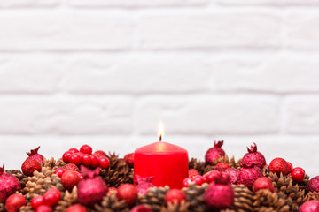 Christmas wreath with red candle, pine cones, on white brick wall background