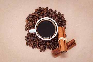 Cup of black coffee, beans, cinnamon sticks on craft paper background