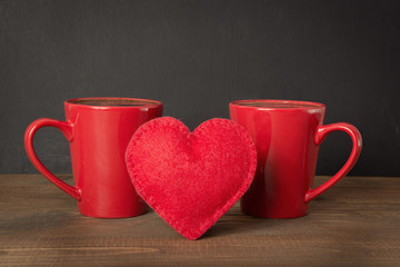 Valentines day composition with red coffee cups and felt heart over wooden board with chalckboard as background. Copy space.