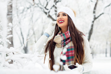 Woman listening music with her mobile phone in first snow