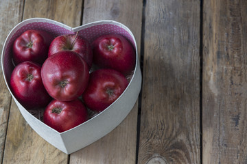 on a wooden background red apples in a box in the shape of a heart