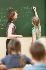 Schoolchildren with teacher in classroom. Pupil solving task and writing on blackboard.