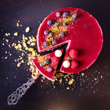 Delicious raspberry cake with fresh strawberries, raspberries, blueberry, currants and pistachios on vintage background. Copy space. Banner