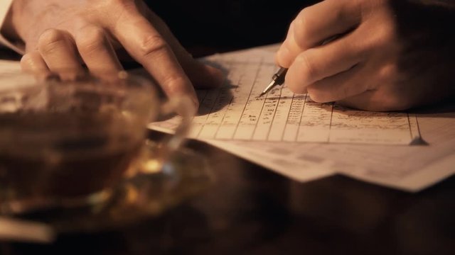Close up dolly scene across hands of a 1930s businessman with fountain pen making entries into a ledger.