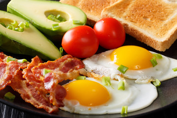 Delicious and hearty meal: two fried eggs with bacon, avocado, toast and tomato macro on a plate. horizontal