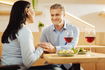 Red wine. Content disabled dark-haired woman and a handsome smiling well-built man sitting in a cafe and holding hands and having romantic dinner