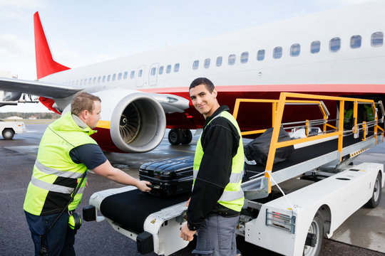 Worker Smiling While Colleague Unloading Luggage On Runway