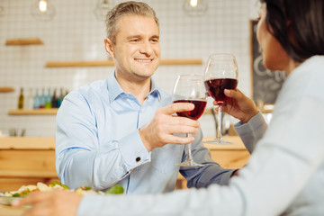 Drinking red wine. Handsome alert blond man and a dark-haired woman sitting together and drinking wine and having dinner
