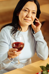 Relaxation. Beautiful content dark-eyed woman smiling and looking in the distance while drinking red wine